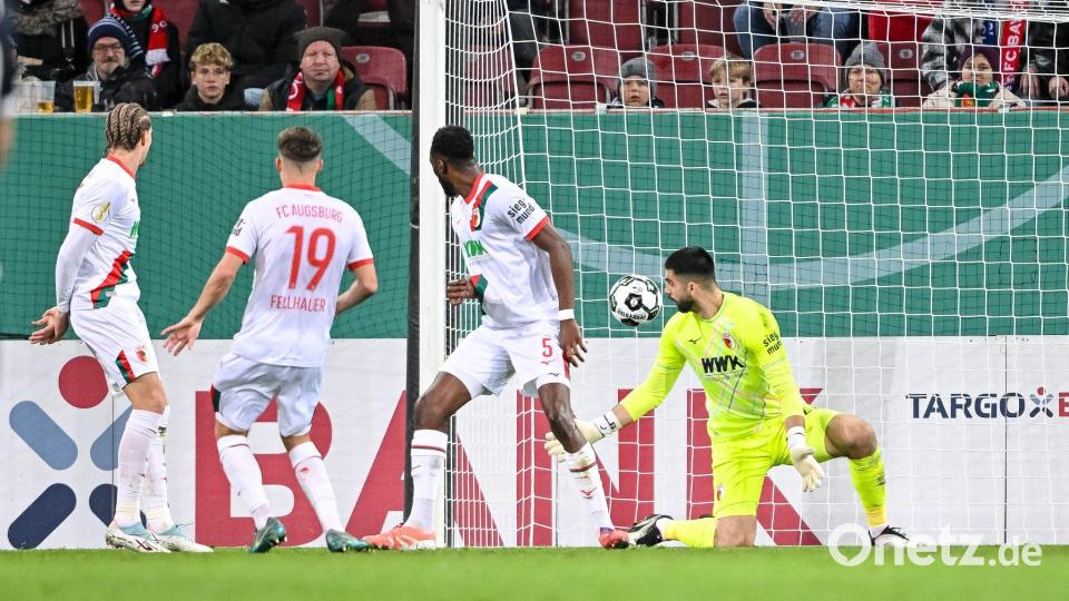 Der Schuss, der zum Augsburger Pokal-K.o. führt. Verteidiger Chrislain Matsima (M) fälscht den Ball auch noch unglücklich und damit unhaltbar ab. Bild: Harry Langer/dpa
