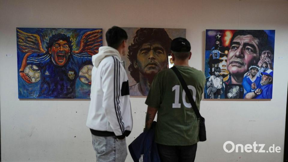 Menschen betrachten eine Kunstausstellung mit Bildern des verstorbenen Fußballstars Maradona. Bild: Natacha Pisarenko/AP/dpa