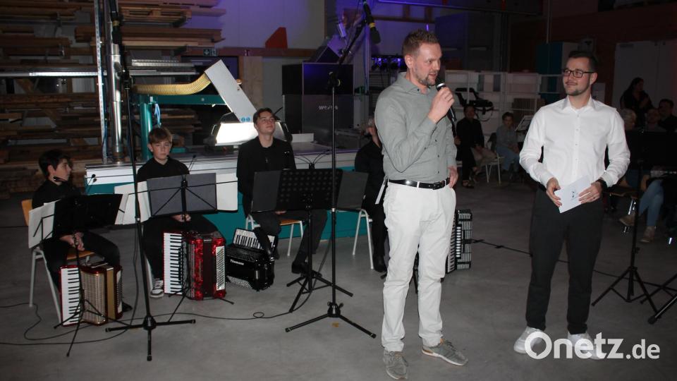 Als Gastgeber begrüßte Schreinereiinhaber Sebastian Hösl (stehend, links) die rund 200 Besucher des Werkstattkonzerts, das Jonas Plössner (rechts) begleitete. Im Hintergrund das Speichersdorfer Akkordeonensemble. Bild: Bernhard Piegsa