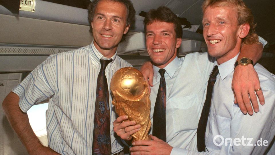 DFB-Teamchef Franz Beckenbauer (l), Kapitän und Mittelfeldspieler Lothar Matthäus (M) und Abwehrspieler Andreas Brehme präsentieren 1990 den zwei Tage zuvor gewonnenen WM-Pokal im Flugzeug auf dem Rückflug von Rom nach Frankfurt. Bild: Wolfgang Eilmes/dpa