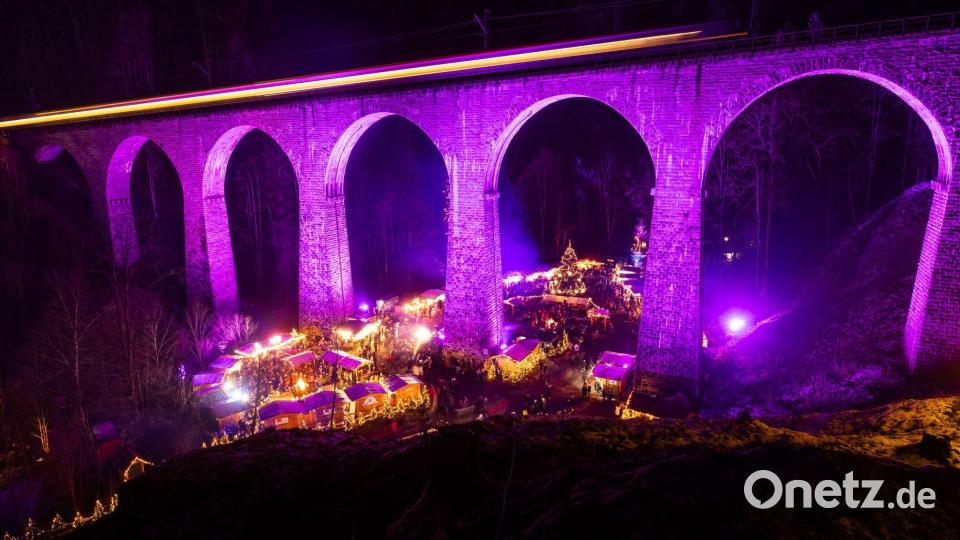 Menschen stehen auf dem Weihnachtsmarkt in der Ravennaschlucht, während über ihnen ein Zug über das Eisenbahn-Viadukt fährt. Bild: Philipp von Ditfurth/dpa