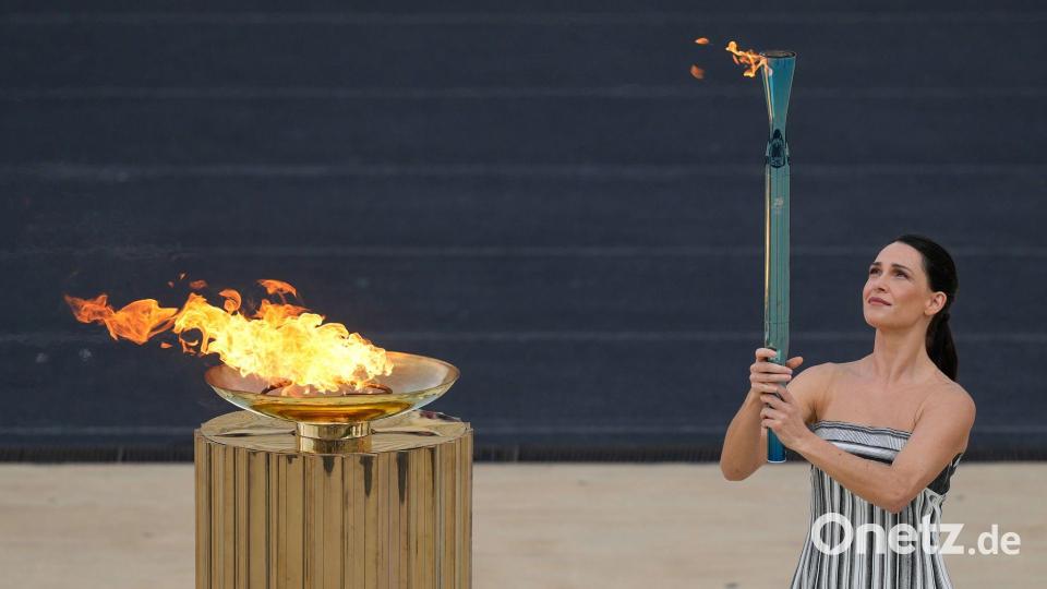 Schauspielerin Mary Mina, in der Rolle der Hohepriesterin, entzündet eine Fackel bei der Zeremonie zur Übergabe der Flamme der Olympischen Winterspiele 2026 im Panathinaikon-Stadion. Bild: Petros Giannakouris/AP/dpa