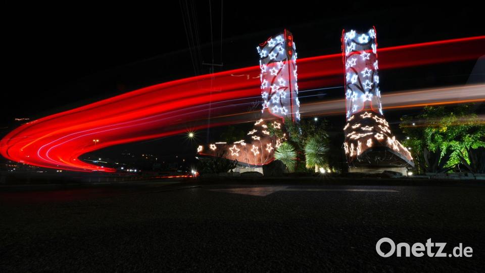 In einer Langzeitbelichtung fahren Fahrzeuge an einem Paar Cowboystiefel vorbei, die 40 Fuß hoch und 30 Fuß lang sind und für die Feiertage mit Lichtern geschmückt wurden. Bild: Eric Gay/AP/dpa