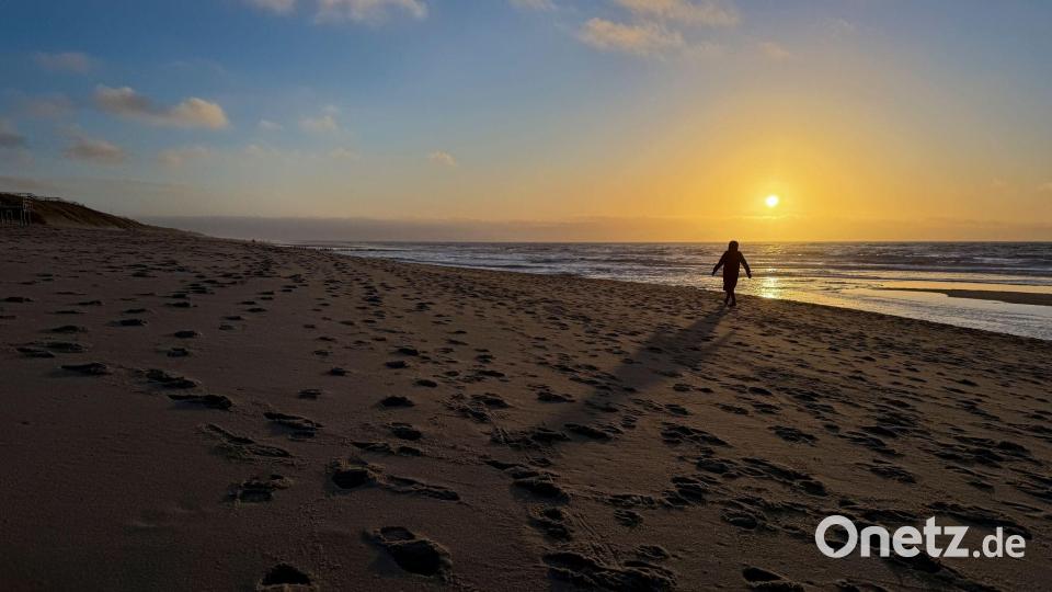 Eine Frau geht im Licht der tief stehenden Sonne am Strand bei Rantum auf Sylt spazieren. Bild: Christian Charisius/dpa