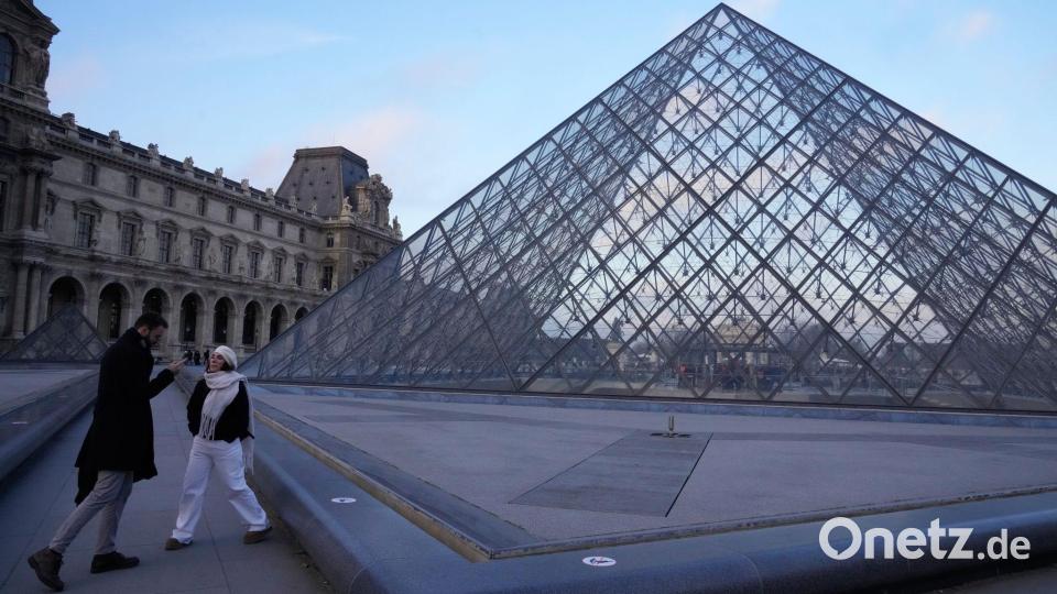 Menschen stehen an der Pyramide des Louvre-Museums am Montagmorgen. Bild: Michel Euler/AP/dpa
