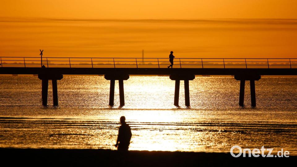 Ein Mann spaziert bei Sonnenaufgang am Altona Pier entlang. Bild: Ye Myo Khant/SOPA Images via ZUMA Press Wire/dpa