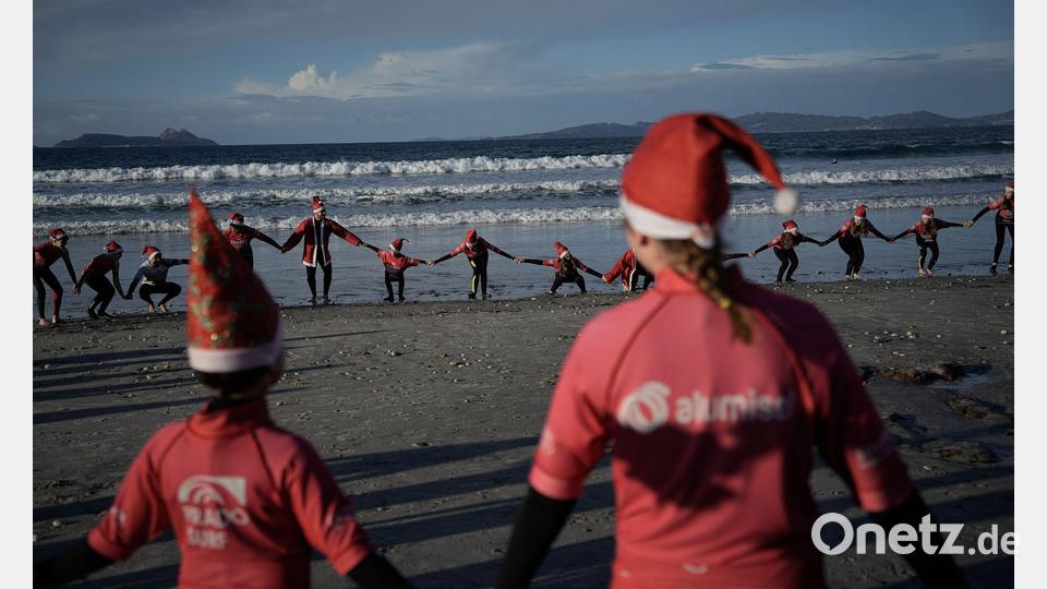Mit Weihnachtsmannmützen verkleidete Menschen surfen während der „Papanoelada Surfera“ (Surfer-Nikolaus-Aktion) am Strand von Patos. Bild: Adrián Irago/EUROPA PRESS/dpa