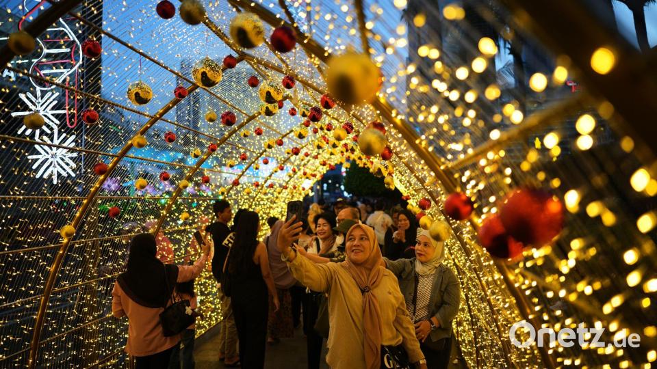 Menschen machen Selfies unter einer Weihnachtsbeleuchtung in Jakarta. Bild: Dita Alangkara/AP/dpa
