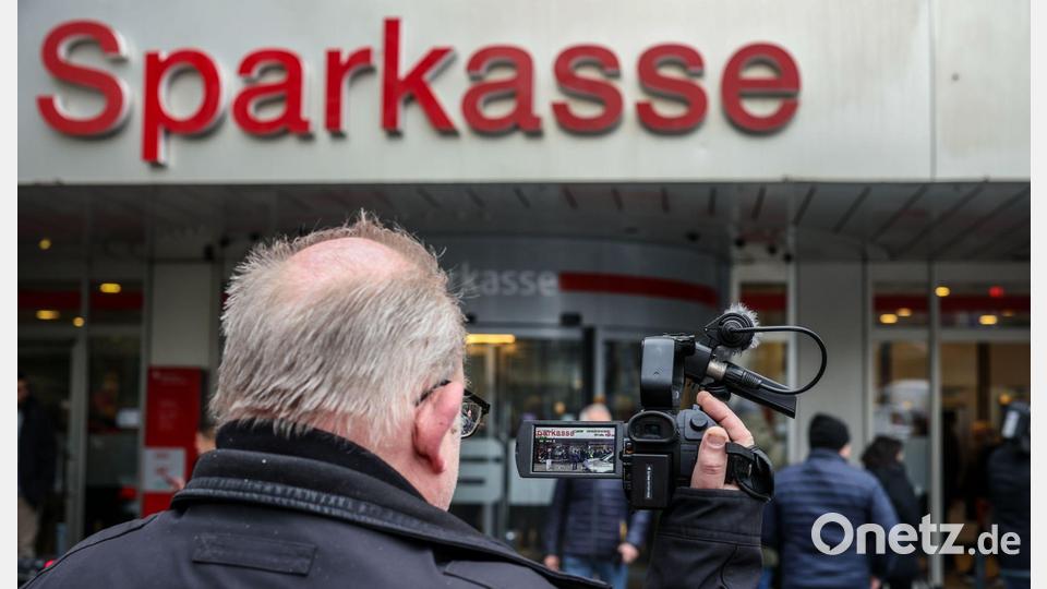 Ein Medienvertreter steht mit einer Kamera vor der Sparkassenfiliale in Buer. Bild: Christoph Reichwein/dpa