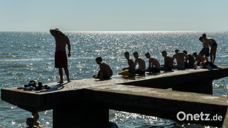 Menschen sitzen auf einem Dock in Montevideo. Bild: Matilde Campodonico/AP/dpa