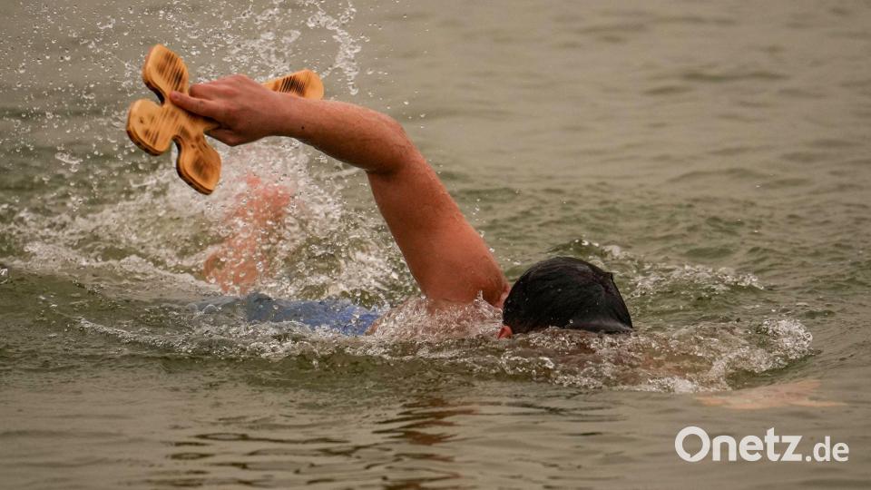 Ein Mann schwimmt mit einem von drei Holzkreuzen, die der orthodoxe Erzbischof Teodosie bei Harsova in die Donau geworfen hat, damit die Menschen sie zurückholen können, während eines Gottesdienstes einen Tag vor dem Dreikönigsfest. Bild: Vadim Ghirda/AP/dpa