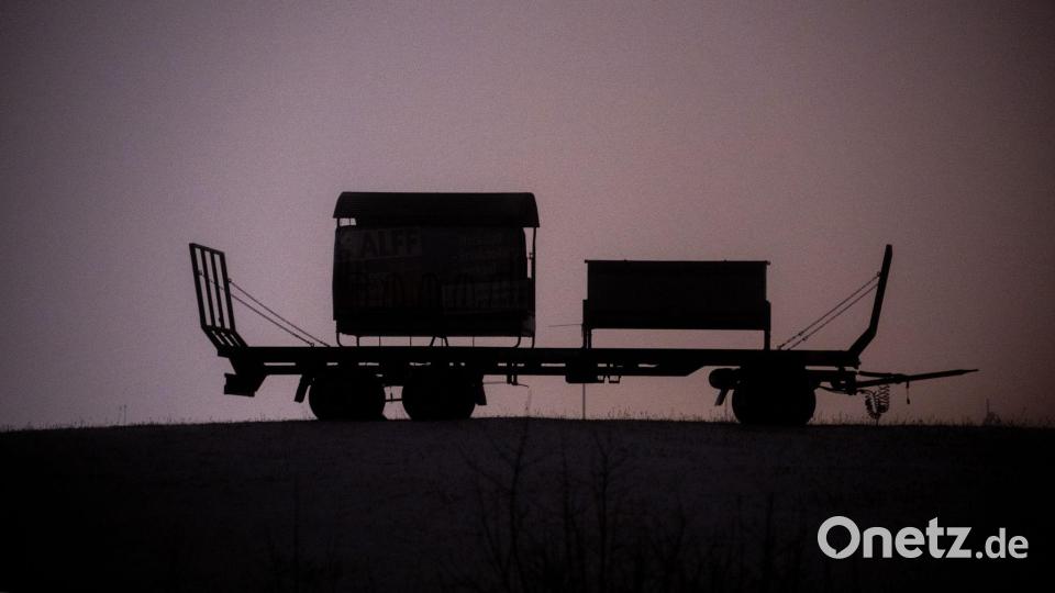 Ein Anhänger steht auf einer schneebedeckten Wiese bei Bitburg und wird von Straßenleuchten erhellt. Bild: Harald Tittel/dpa