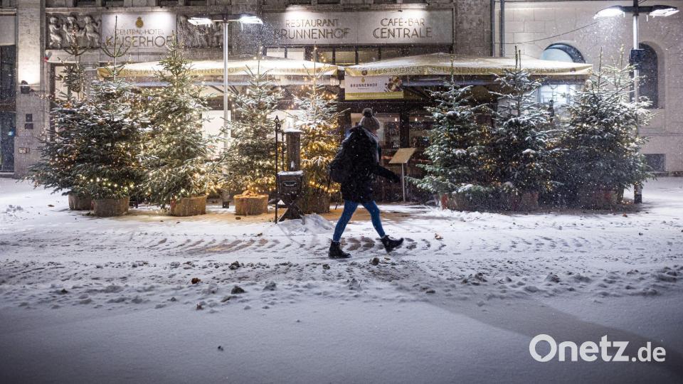 Eine Passantin geht am frühen Morgen im dichten Schneefall an Weihnachtsbäumen im Zentrum entlang. Bild: Moritz Frankenberg/dpa