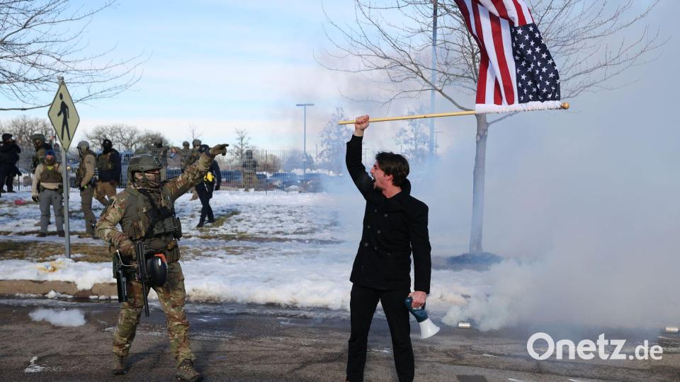 Ein Protestierender mit einer amerikanischen Flagge steht einem ICE-Beamten gegenüber. Bild: Adam Bettcher/AP/dpa