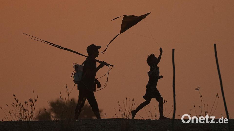 Ein Junge (r) lässt einen Drachen steigen, während er mit seinem Vater nach dem Fischen am Stadtrand von Phnom Penh nach Hause geht. Bild: Heng Sinith/AP/dpa