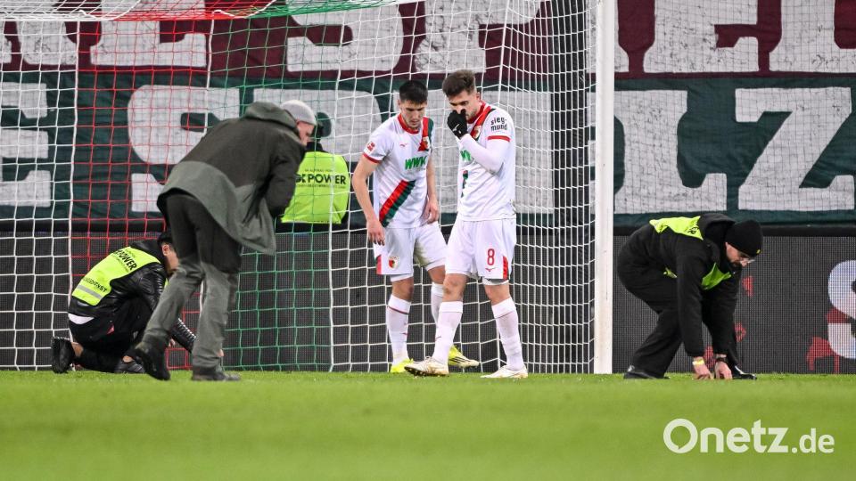 Spieler und Ordner sammeln nach dem Fanprotest Gegenstände vom Rasen. Bild: Harry Langer/dpa