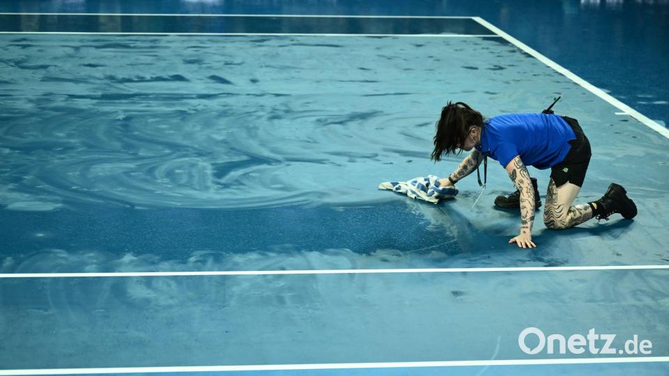 Australian Open: Eine Person trocknet den Platz mit einem Handtuch, nachdem das Spiel aufgrund des Regens unterbrochen wurde. Bild: Joel Carrett/AAP/dpa