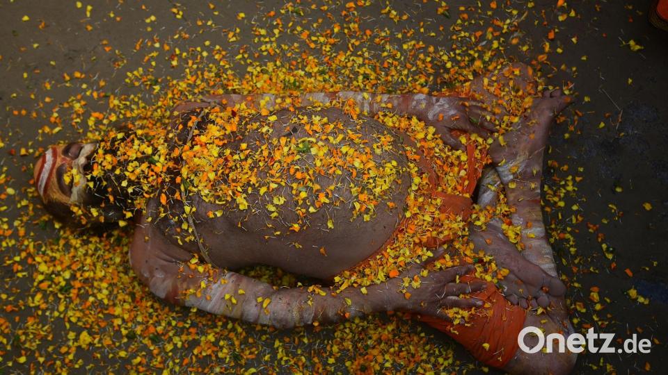Bei einem hinduistischen Frühlingsfest in Indien liegt ein Sadhu mit Blütenblättern bedeckt auf der Straße. Bild: Prabhat Kumar Verma/ZUMA Press Wire/dpa