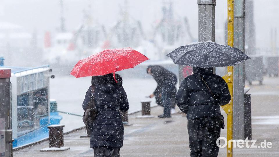 Menschen schützen sich vor Schneefall mit Regenschirmen bei einem Spaziergang an den Landungsbrücken am Hamburger Hafen. Bild: Bodo Marks/dpa