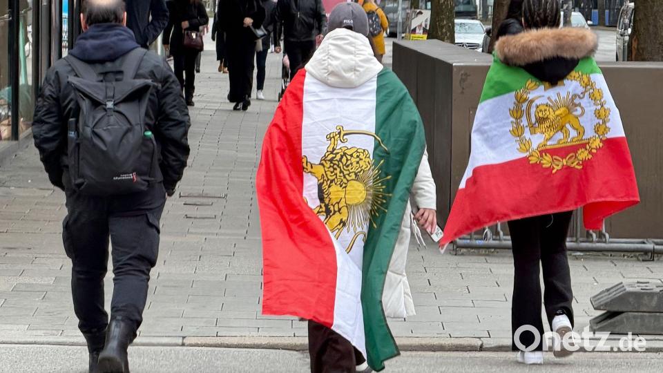 Menschen, die verschiedene ehemalige Flaggen des Iran umhaben, gehen durch die Münchner Innenstadt. Bild: Marijan Murat/dpa