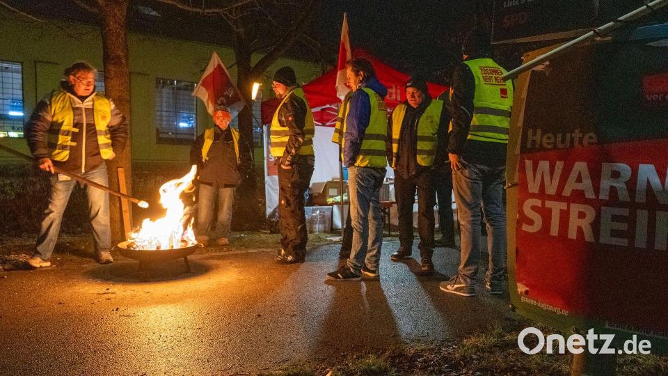 Streikende in Warnwesten wärmen sich in Augsburg an einem Feuer während eines Warnstreiks im ÖPNV. Bild: Stefan Puchner/dpa