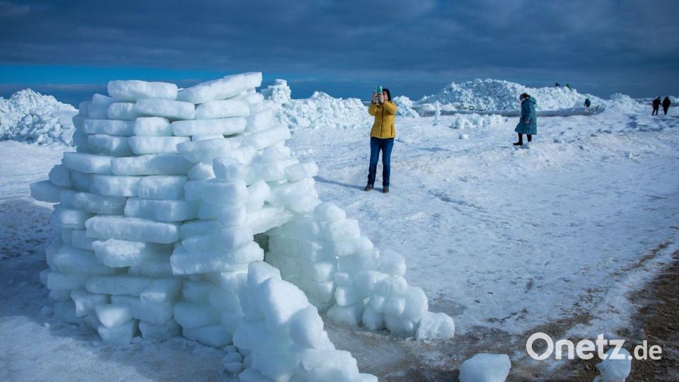 Eine Frau fotografiert ein aus Eisstücken gebautes Iglu vor meterhohen Eisbergen am Ostseestrand auf der Insel Usedom. Bild: Jens Büttner/dpa