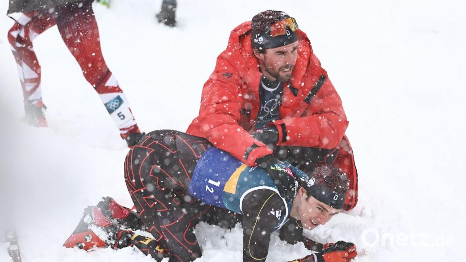 Vinzenz Geiger liegt im Schnee und wird von Teamkollege Johannes Rydzek getröstet. Bild: Daniel Karmann/dpa