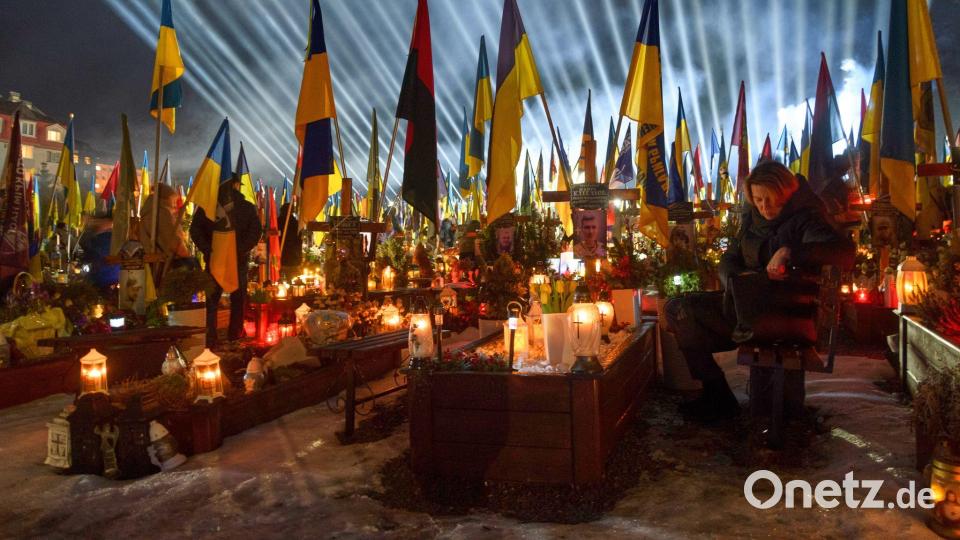 Flutlichter leuchten in Lwiw über den Gräbern der gefallener Soldaten, während Menschen am Vorabend des vierten Jahrestages der russischen Invasion Kerzen anzünden. Bild: Mykola Tys/AP/dpa