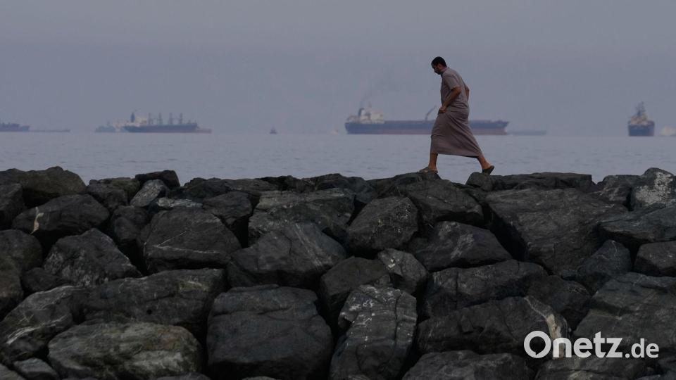 Ein Mann geht auf den Felsen am Ufer in Chaur Fakkan in den Vereinigten Arabischen Emiraten, während im Hintergrund Öltanker und Frachtschiffe in der Straße von Hormus aufgereiht sind. Bild: Altaf Qadri/AP/dpa
