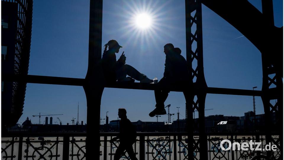 Ein Pärchen sitzt in der Sonne auf dem Geländer der Hackerbrücke in München. Bild: Peter Kneffel/dpa