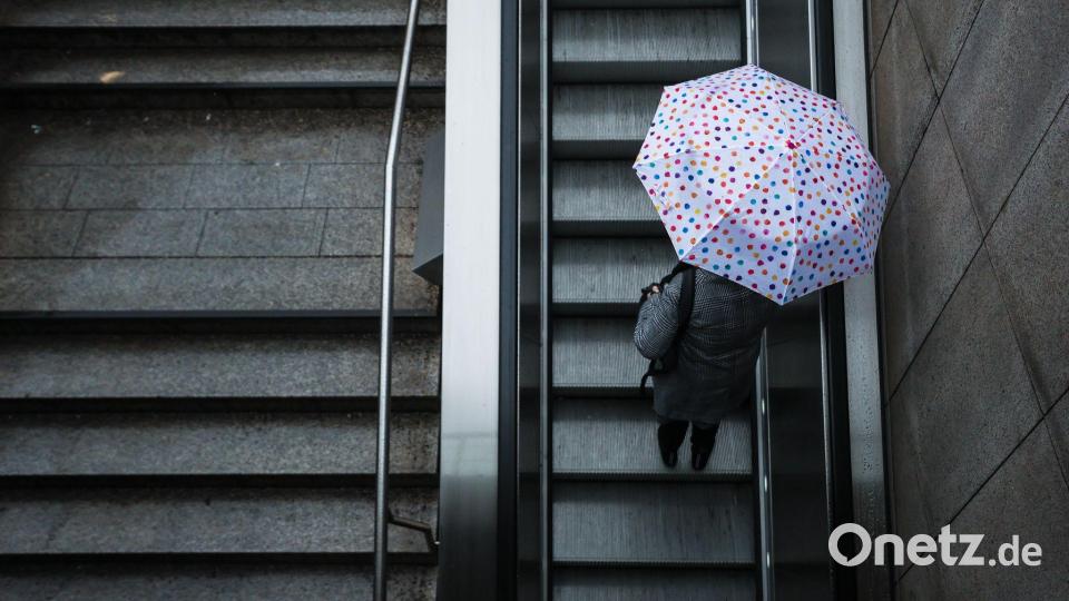 Eine Frau fährt mit ihrem Regenschirm eine Rolltreppe hinauf. Das Wetter soll in der Region Stuttgart in den nächsten Tagen wechselhaft bleiben. Bild: Christoph Schmidt/dpa