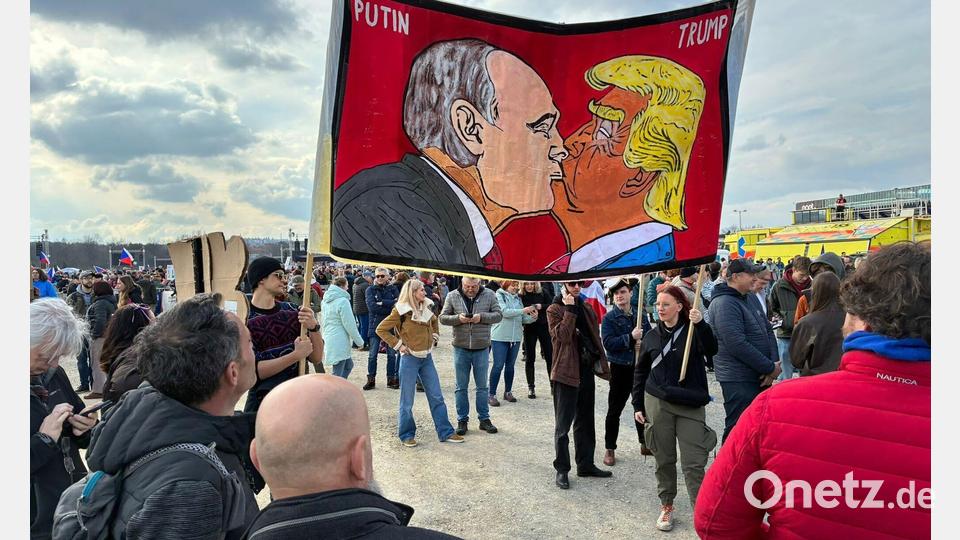 Demonstranten halten bei einer Kundgebung des Bündnisses „Eine Million Augenblicke für Demokratie“ ein Banner, auf dem sich stilisiert US-Präsident Trump und Russlands Präsident Putin küssen. Bild: Michael Heitmann/dpa