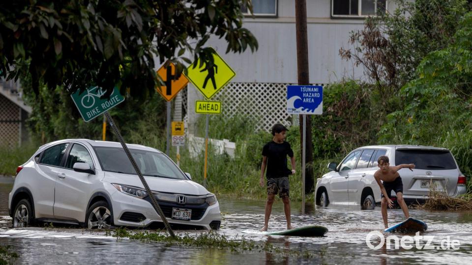 Zwei Jugendliche surfen in Waialua neben einem liegengebliebenen Fahrzeug im Hochwasser. Bild: Stephen Lam/San Francisco Chronicle via AP/dpa