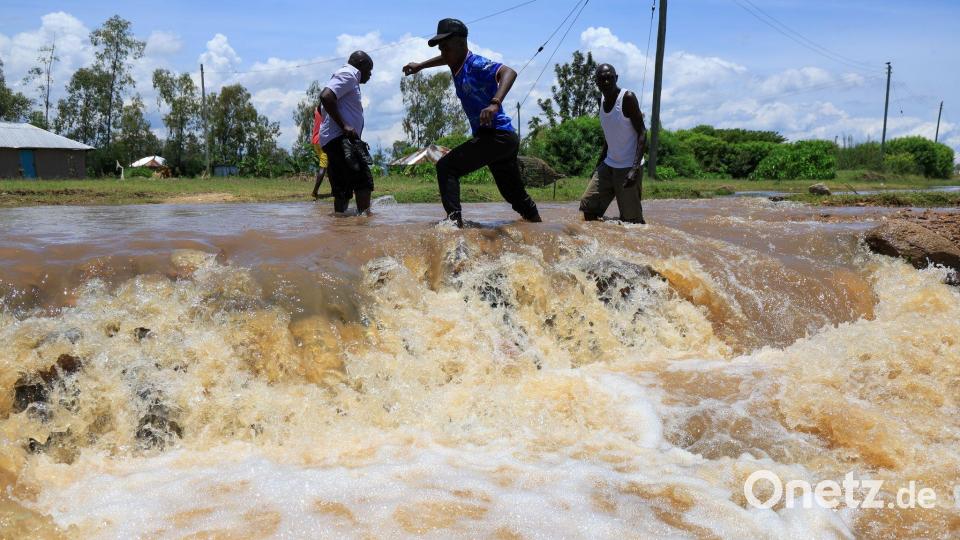 Menschen überqueren einen überfluteten Straßenabschnitt nach schweren Regenfällen in Ahero, Kenia. Bild: Andrew Kasuku/AP/dpa