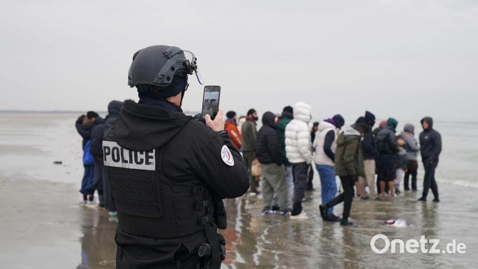 Ein Mitglied der französischen Behörden filmt eine Gruppe von Menschen, bei denen es sich vermutlich um Migranten handelt, die am Strand von Gravelines, Frankreich, warten, während sie versuchen, ein kleines Boot zu besteigen, um den Ärmelkanal zu überqueren. Bild: Gareth Fuller/PA Wire/dpa