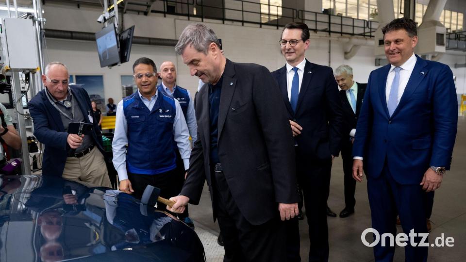 Bald fährt ein BMW herum, dessen Logo auf der Motorhaube von Markus Söder per Hammer angebracht wurde. Bild: Sven Hoppe/dpa
