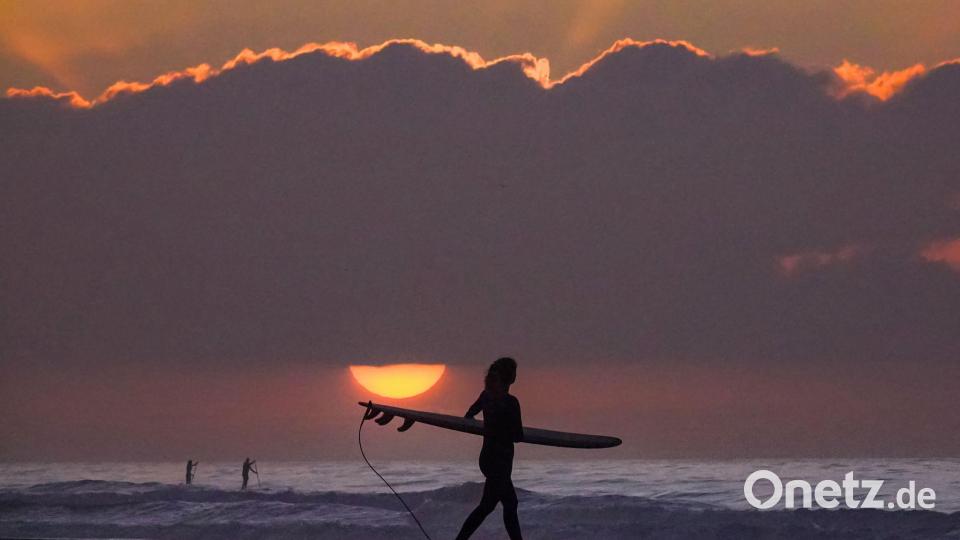 Eine Surferin trägt ihr Surfbrett in Richtung Meer. Bild: Richard Ellis/ZUMA Press Wire/dpa