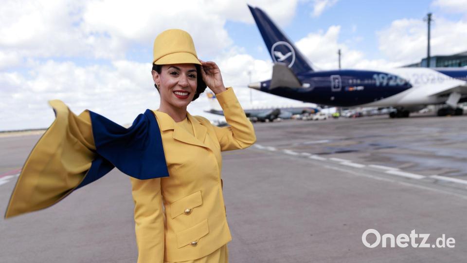 Eine Hostess trägt eine frühere Lufthansa-Uniform vor einem Passagierflugzeug der Lufthansa auf dem Flughafen Berlin-Brandenburg (BER) bei der Feier von Lufthansa zum 100. Jahrestag des Erstflugs. Bild: Carsten Koall/dpa