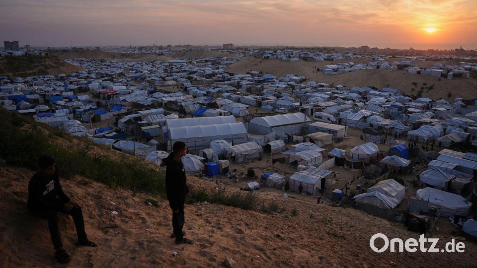 Palästinensische Jugendliche schauen im südlichen Gazastreifen dem Sonnenuntergang zu, als sie in einem behelfsmäßigen Lager für Vertriebene vor Zelten stehen. Bild: Abdel Kareem Hana/AP/dpa