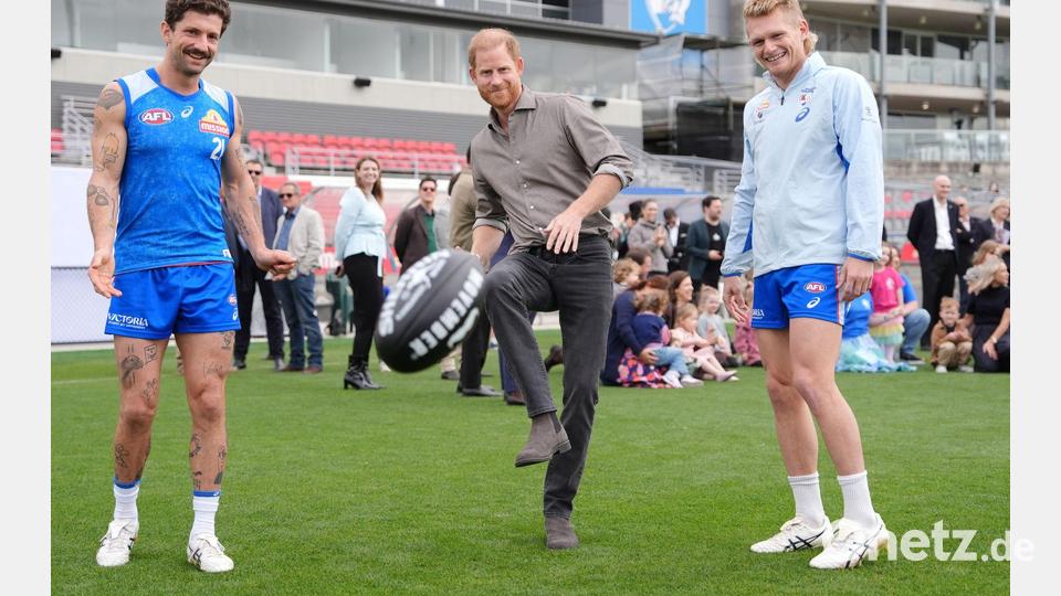 Prinz Harry (M), Herzog von Sussex, kickt einen Football. Bild: Jonathan Brady/Pool PA/AP/dpa
