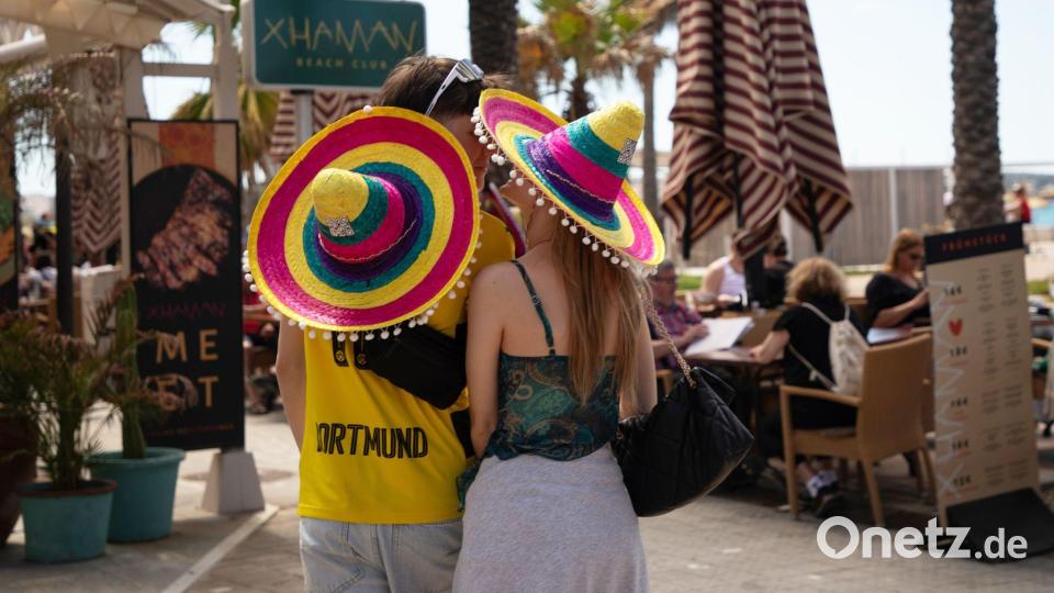 Touristen mit bunten Hüten stehen beim Start der Ballermann-Saison auf Mallorca an einer Bar. Bild: Clara Margais/dpa