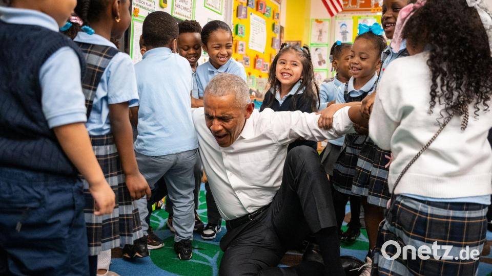 Der frühere US-Präsident Barack Obama lässt sich beim Aufstehen von Kindern hochheben. Bild: Angelina Katsanis/AP/dpa
