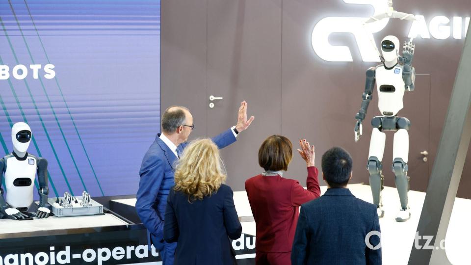 Bundeskanzler Friedrich Merz winkt einem Roboter zu – die Zukunft winkt zurück. Bild: Michael Matthey/dpa