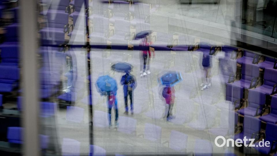 Passanten mit Regenschirmen spiegeln sich in den Fenstern vor dem Plenarsaal des Bundestags. Bild: Kay Nietfeld/dpa