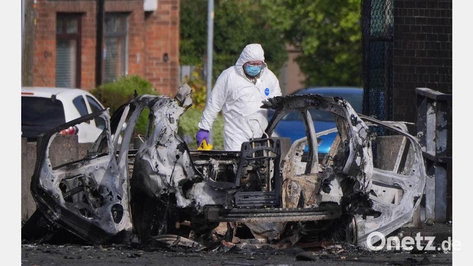 Nach einer Explosion vor einer Polizeistation steht ein Ermittler neben einem zerstörten Auto in Dunmurry, nahe Belfast in Nordirland. Bild: Niall Carson/PA Wire/dpa