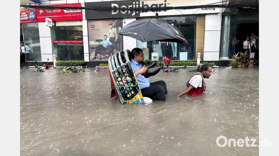 Die Schuhe bleiben trocken: Ein Mann lässt sich in Bangladesch in einer Rikscha durch eine überflutete Straße fahren. Bild: -/XinHua/dpa