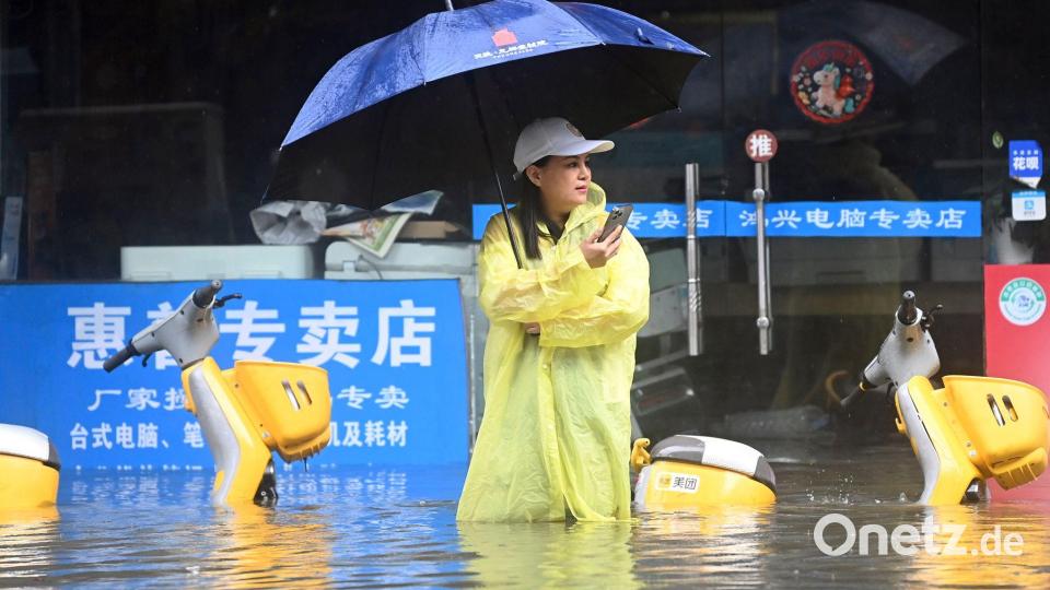 Eine Frau steht in Qinzhou auf einer mit Wasser vollgelaufenen Straße. Bild: Zhang Ailin/XinHua/dpa