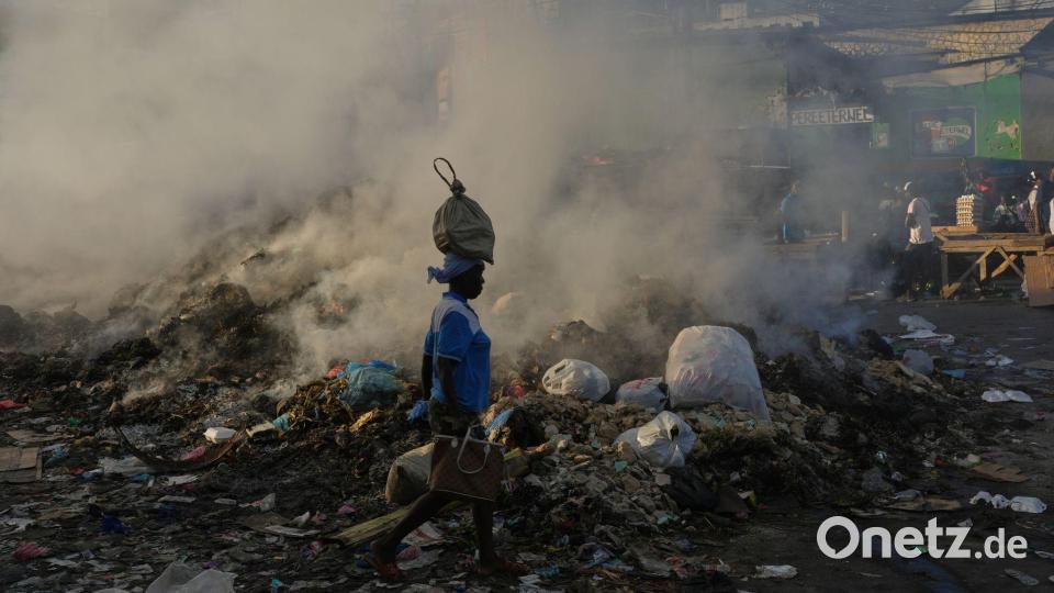 Eine Frau, die eine Tasche auf dem Kopf trägt, geht im Stadtteil Petion-Ville von Port-au-Prince an schwelendem Müll vorbei. Bild: Odelyn Joseph/AP/dpa