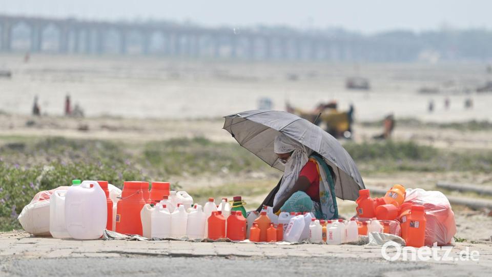 Hitze in Indien: Von Kanistern umgeben wartet ein Verkäufer mit einem Schirm in Prayagraj auf Kunden. Bild: Prabhat Kumar Verma/ZUMA Press Wire/dpa