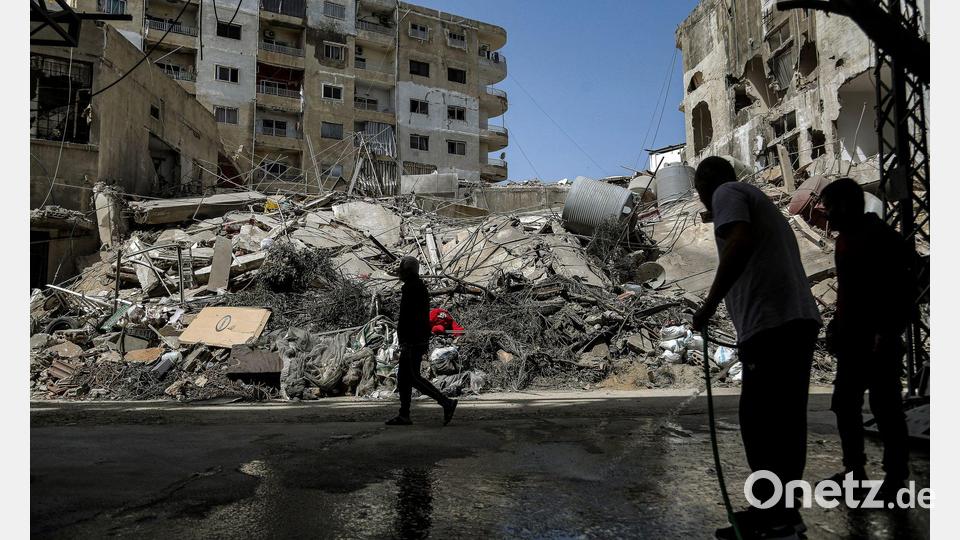 Ein Mann spritzt nach israelischen Luftangriffen im Libanon Wasser auf eine Straße vor zerstörten Gebäuden. Bild: Marwan Naamani/dpa